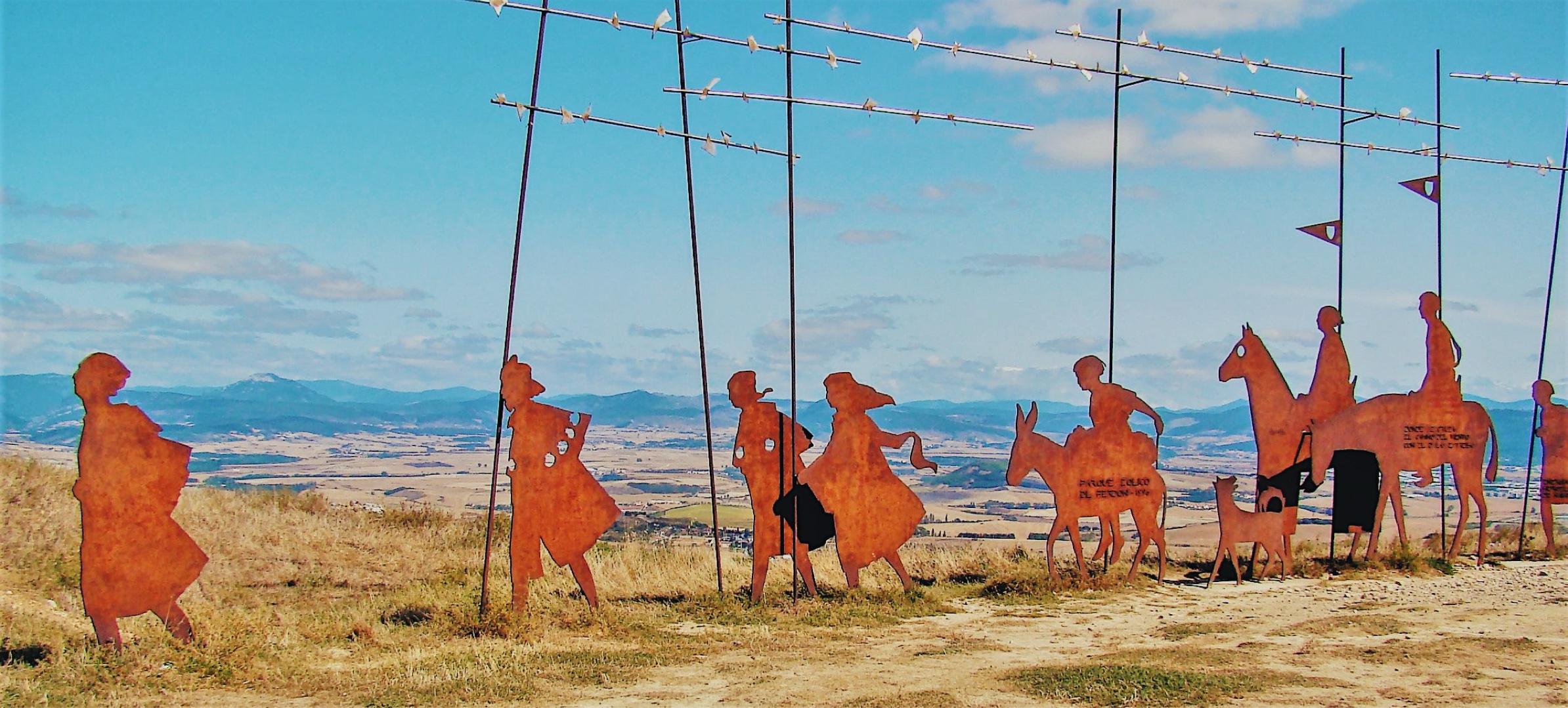 The bronze pilgrim sculptures on the ridge at the Alto del Perdón, wind turbines behind