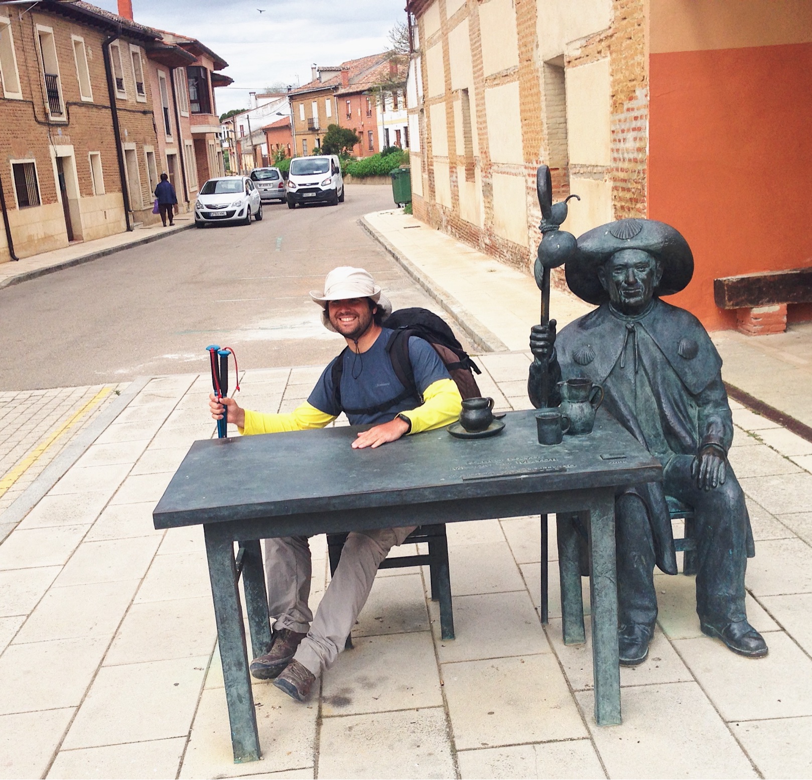 A pilgrim sits at a bronze table with a statue of a medieval pilgrim